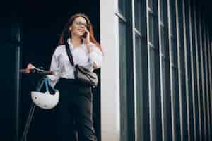 Free photo young business woman riding scooter and using phone