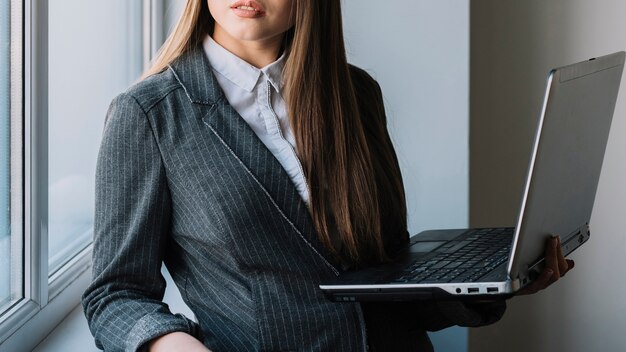 Young business woman standing at window with laptop