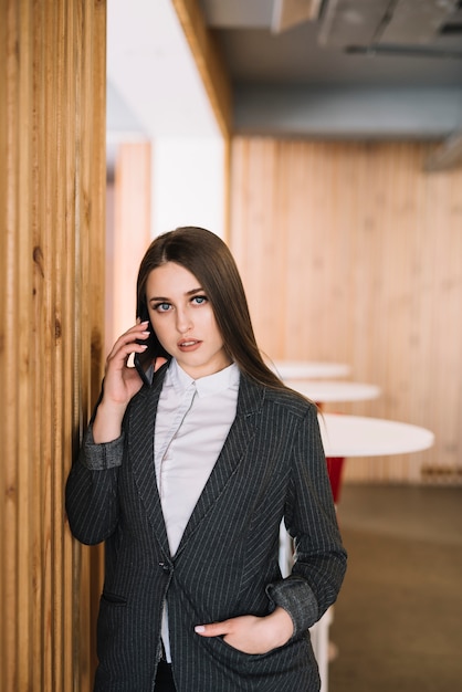 Young business woman talking by phone at wall