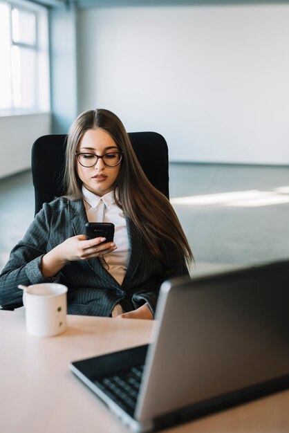 Young business woman using smartphone at table with laptop