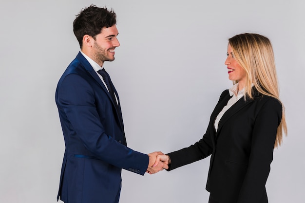 Free photo young businessman and businesswoman shaking each other's hand against grey backdrop