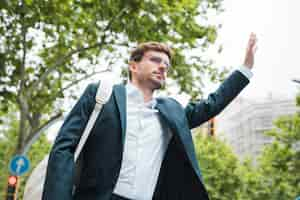 Free photo young businessman carrying white backpack on his shoulder hitchhiking