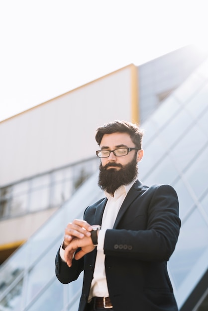 Young businessman checking time standing against office building