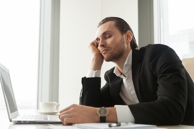 Young businessman dozed in front of laptop at work.