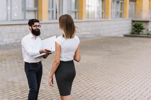 Young businessman giving paper document to businesswoman standing at outdoors