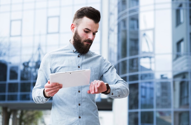 Free photo young businessman holding digital tablet in hand checking time