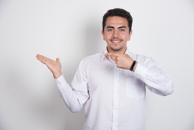 Young businessman pointing his side on white background.