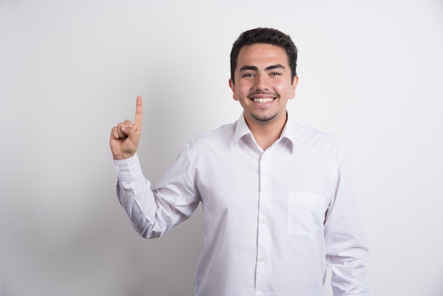 Young businessman pointing upside on white background.