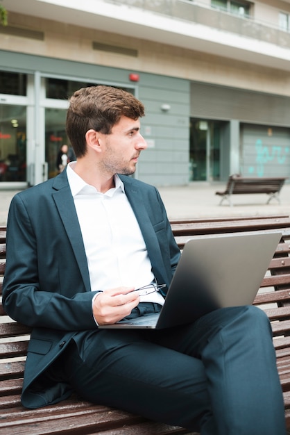 Free photo young businessman sitting on bench with laptop