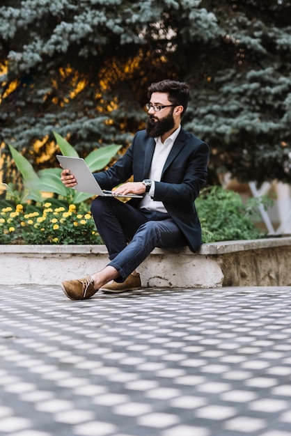 Young businessman sitting at outdoors using laptop