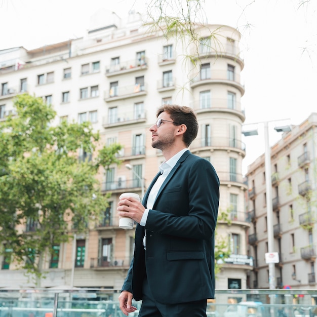 Free photo young businessman standing in front of building holding coffee cup in hand