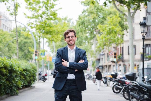 Young businessman standing on street with his arm crossed looking at camera