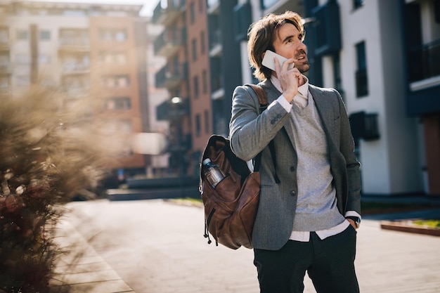 Free photo young businessman talking on cell phone while standing on the street.