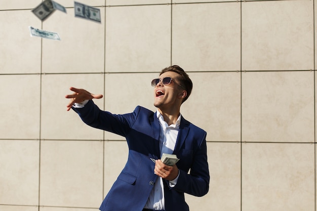 Free photo young businessman throughs around dollars and dances on the street