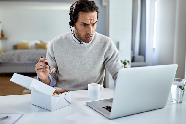 Young businessman using computer while having lunch break at home