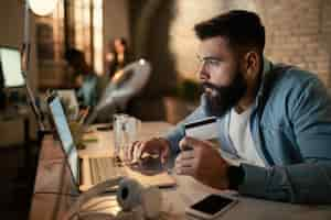 Free photo young businessman using laptop and credit card while buying on the internet at night in the office