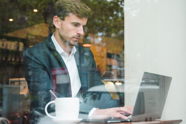 Free photo young businessman using laptop with cup of coffee in cafe