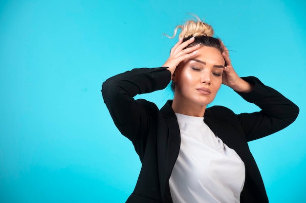 Young businesswoman in bun wearing black blazer holding her head.