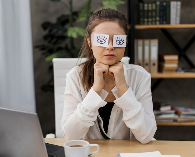 Young businesswoman covering her eyes with drawn eyes on paper