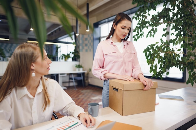 Young businesswoman holding box of personal belongings about to leave office after quitting job