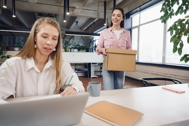 Young businesswoman holding box of personal belongings about to leave office after quitting job