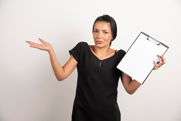 Young businesswoman holding clipboard on white wall.