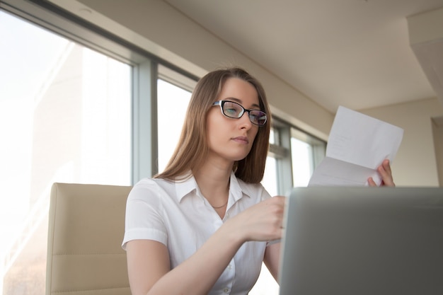 Young businesswoman reading letter at workplace