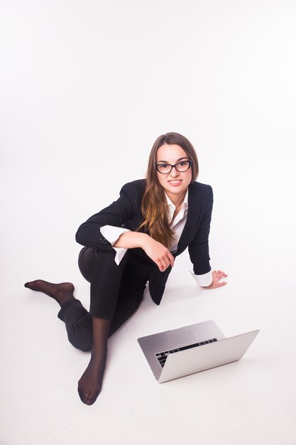 Young businesswoman sitting on floor and using laptop isolated on white wall