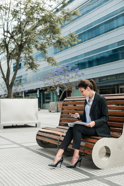 Young businesswoman sitting outside the building looking at mobile phone