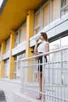 Free photo young businesswoman standing in balcony drinking coffee holding smartphone in hand