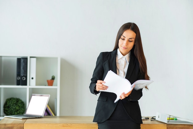 Young businesswoman standing in front of office desk reading documents