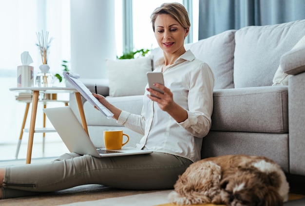 Free photo young businesswoman texting on smart phone while sitting on the floor and working at home her dog is sleeping next to her