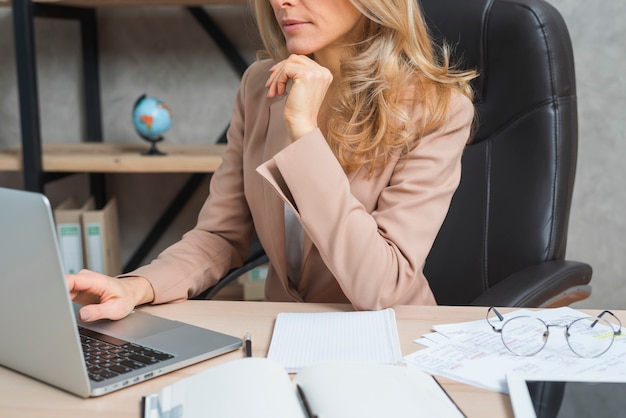 Young businesswoman using laptop with diary and documents at workplace