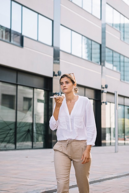 Free photo young businesswoman walking near the office building talking on mobile phone