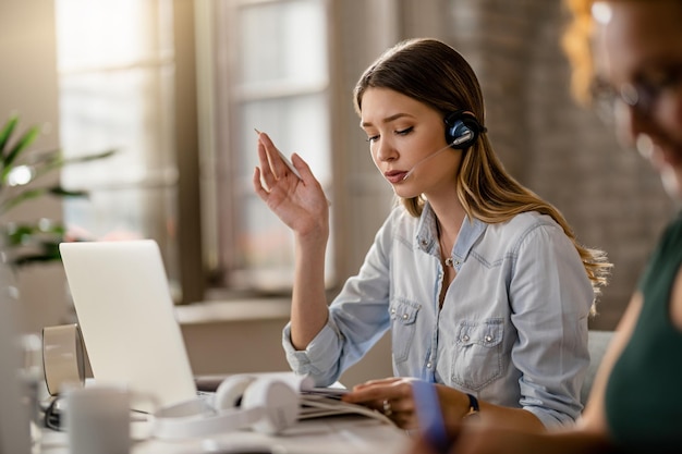 Young businesswoman wearing headset and communicating with a client while going through paperwork in the office