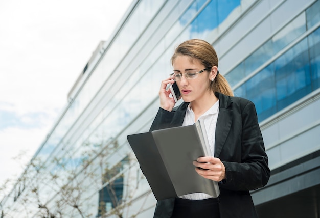 Young businesswoman while talking on cell phone looking at the folder