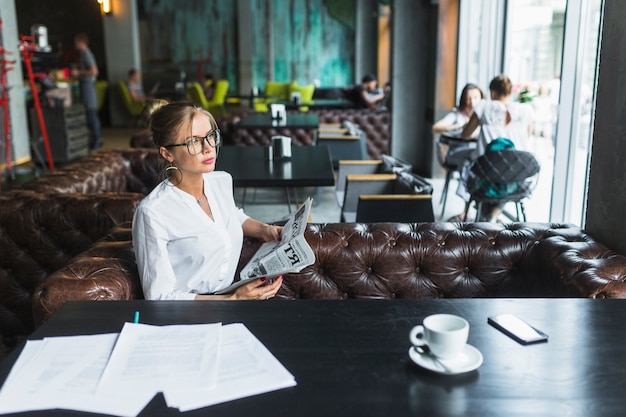 Young businesswoman with newspaper sitting in caf�