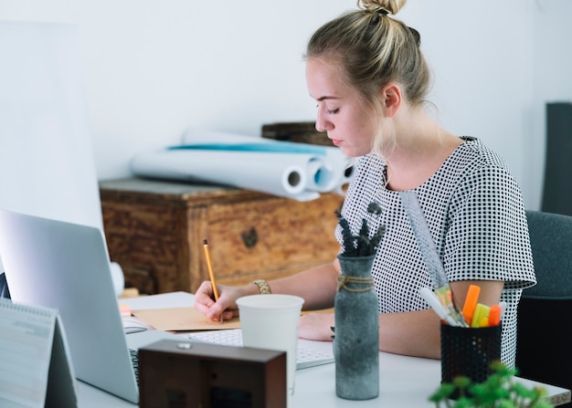 Free Photo young businesswoman writing on paper over the desk