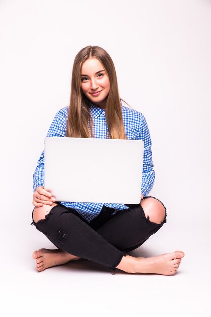 Young casual woman sitting down smiling holding laptop isolated on white wall