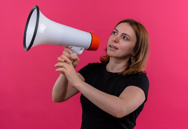 Young casual woman talking by speaker looking at left side on isolated pink wall