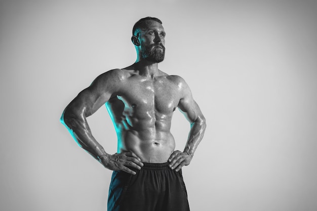 Young caucasian bodybuilder training over studio background in neon light. Muscular male model resting after cross-fit exercises. Concept of sport, bodybuilding, healthy lifestyle, motion and action.