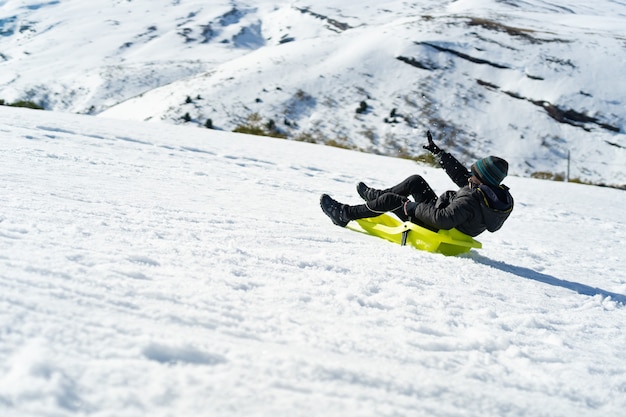 Free Photo young caucasian boy playing with a sled on the mountain covered with snow