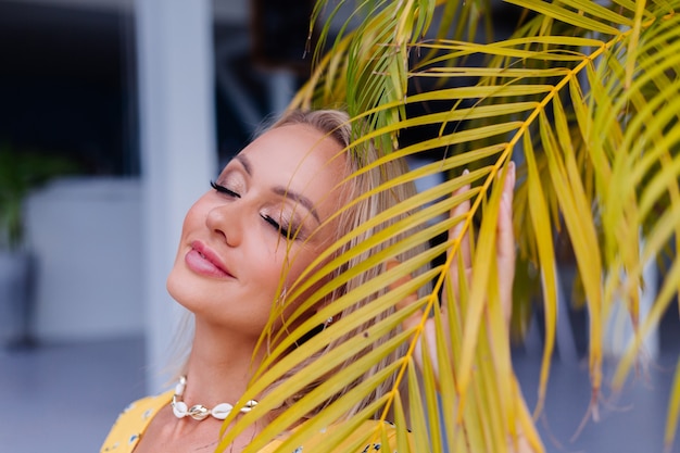 Young caucasian calm happy pretty woman with bright evening makeup wearing summer yellow dress and sea shell necklace