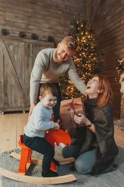 Young caucasian family mom dad son near fireplace christmas tree