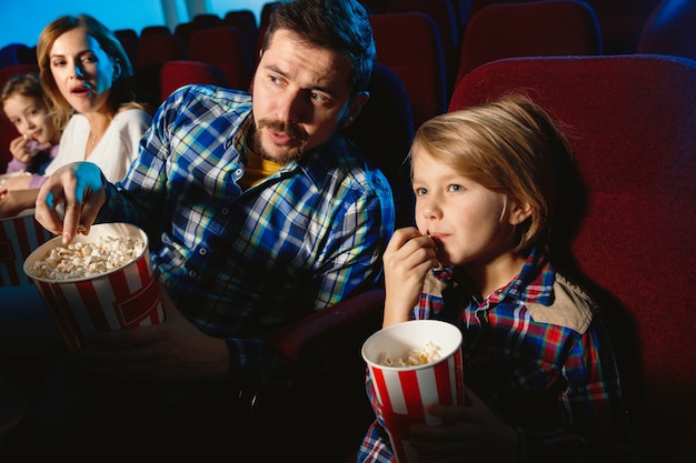 Free photo young caucasian family watching a film at a movie theater, house or cinema. look expressive, astonished and emotional. sitting alone and having fun. relation, love, family, childhood, weekend time.