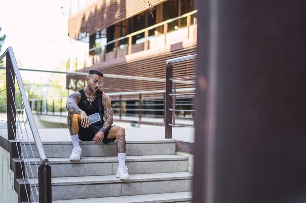 Young caucasian guy with cool tattoos and glasses sitting on the stair