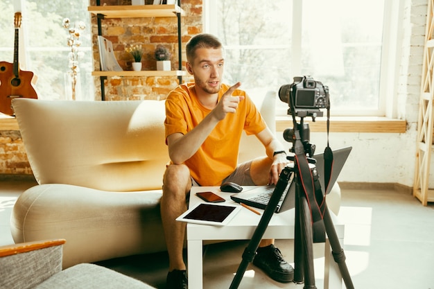 Free photo young caucasian male blogger with professional camera recording video review of gadgets at home. blogging, videoblog, vlogging. man making vlog or live stream about photo or technical novelty.