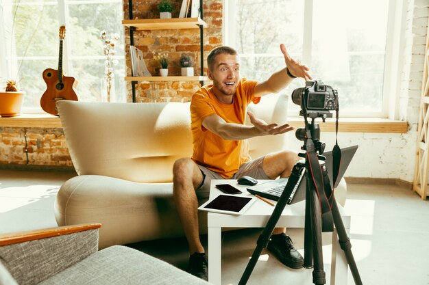 Young caucasian male blogger with professional camera recording video review of gadgets at home. Blogging, videoblog, vlogging. Man making vlog or live stream about photo or technical novelty.