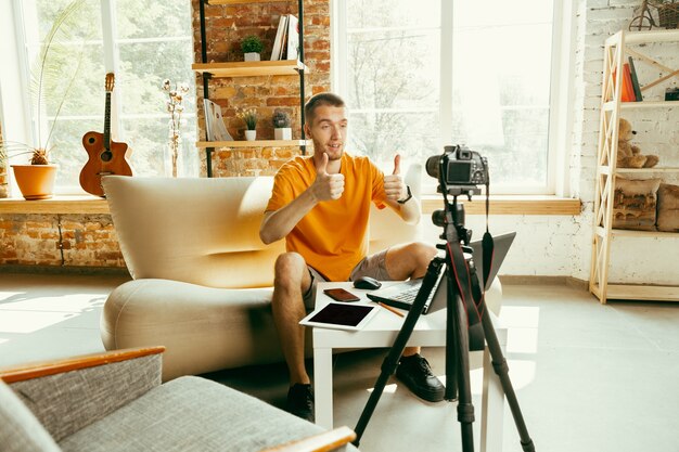 Young caucasian male blogger with professional camera recording video review of gadgets at home