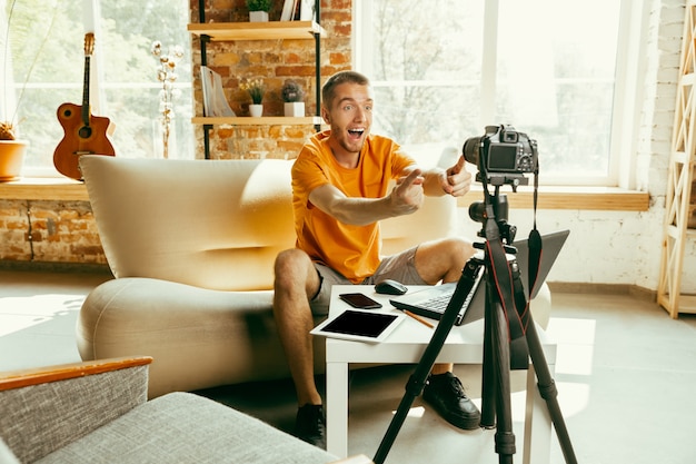 Young caucasian male blogger with professional camera recording video review of gadgets at home